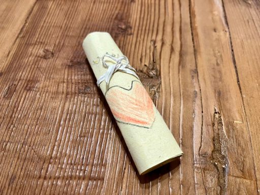 Wunschrolle aus grünem Papier mit einem rosa Blatt, auf einem Holzuntergrund platziert.