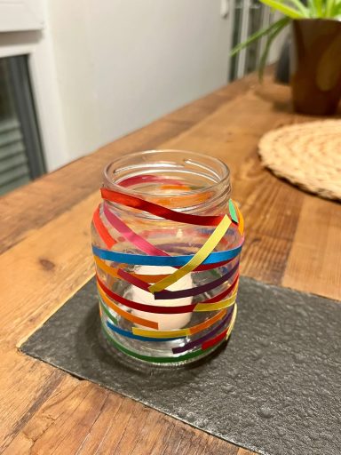 Ein Glas mit bunten Papierstreifen auf einem Holztisch.