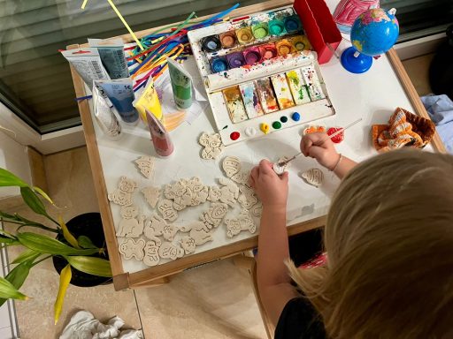 Ein Kind malt und bastelt mit Farben und Materialien an einem Tisch.